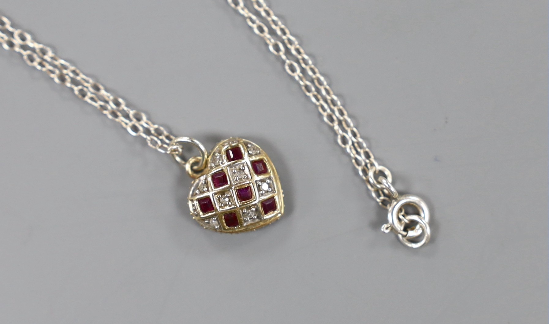 A modern yellow metal ruby and diamond set heart shaped pendant, 11mm,on a 925 chain.